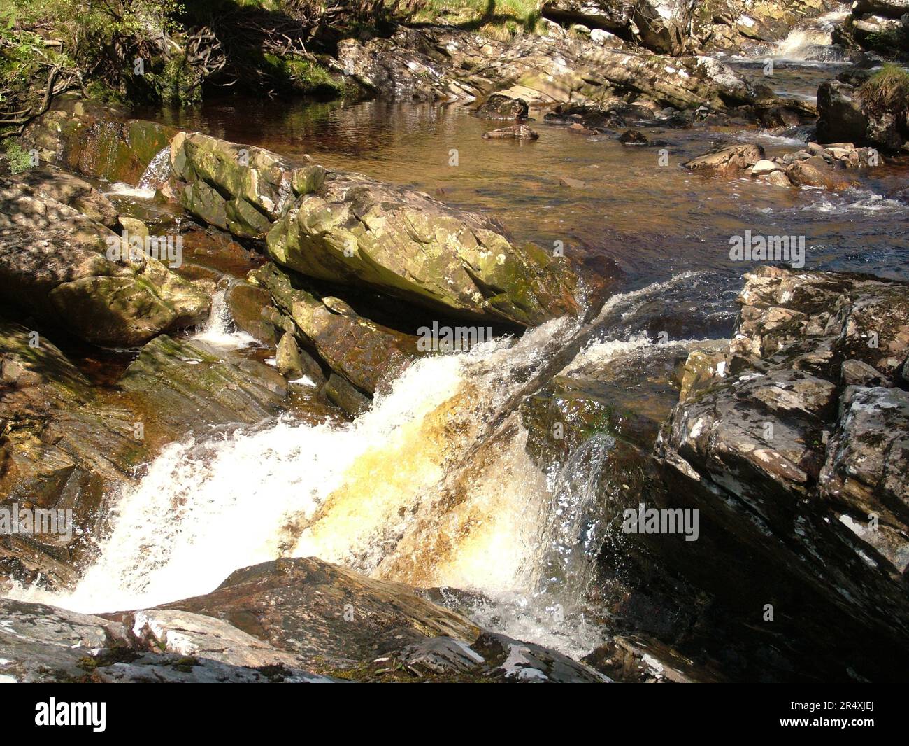 Acqua colorata di torba che scorre su una cascata formata dagli strati inclinati di antiche rocce di un torrente nelle Highlands della Scozia. Foto Stock Acqua colorata di torba che scorre su una cascata formata dagli strati inclinati di antiche rocce di un torrente nelle Highlands della Scozia. Foto Stock