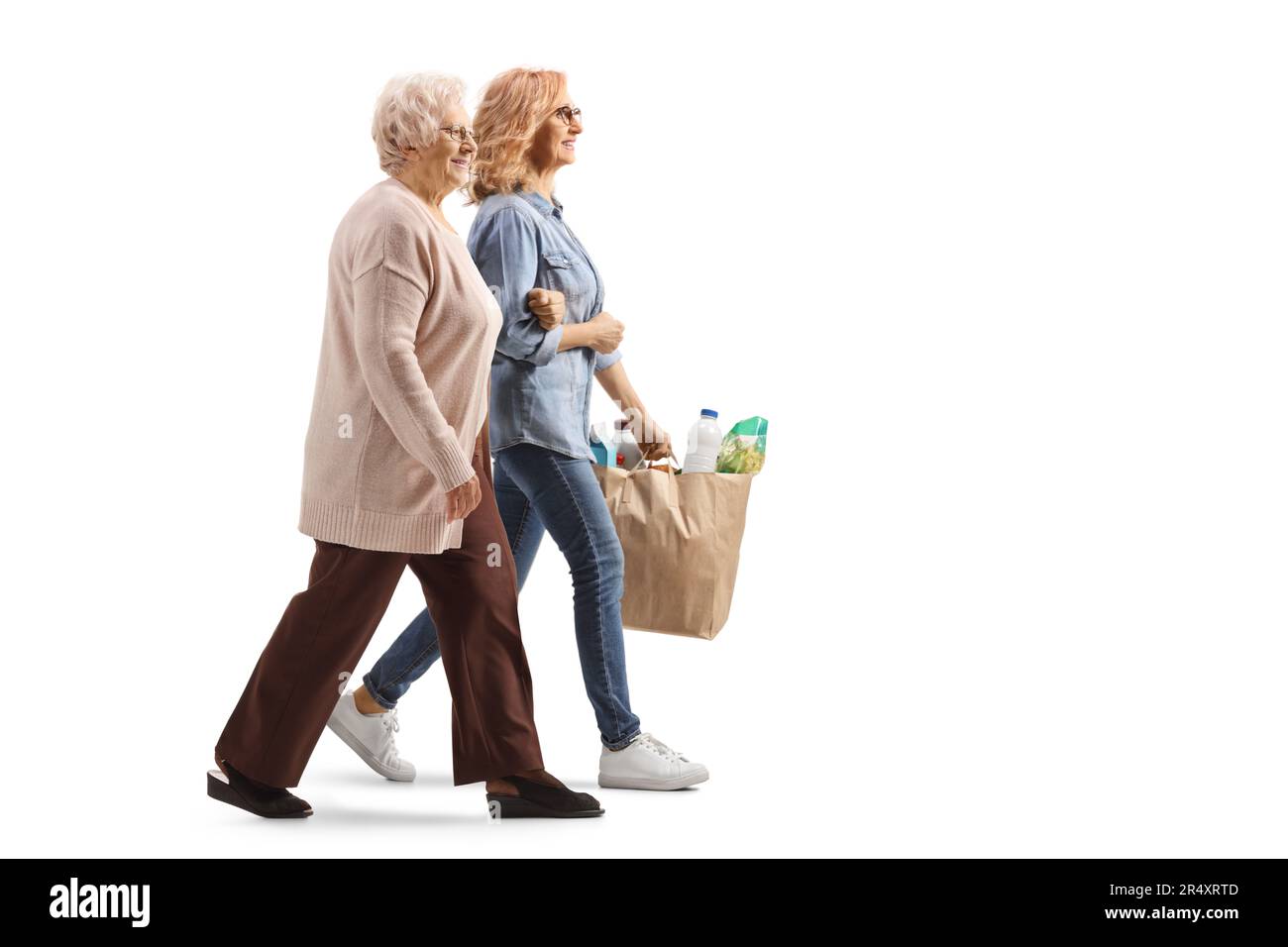 Profilo a tutta lunghezza di una donna che aiuta una donna anziana e porta borse di spesa isolato su sfondo bianco Foto Stock