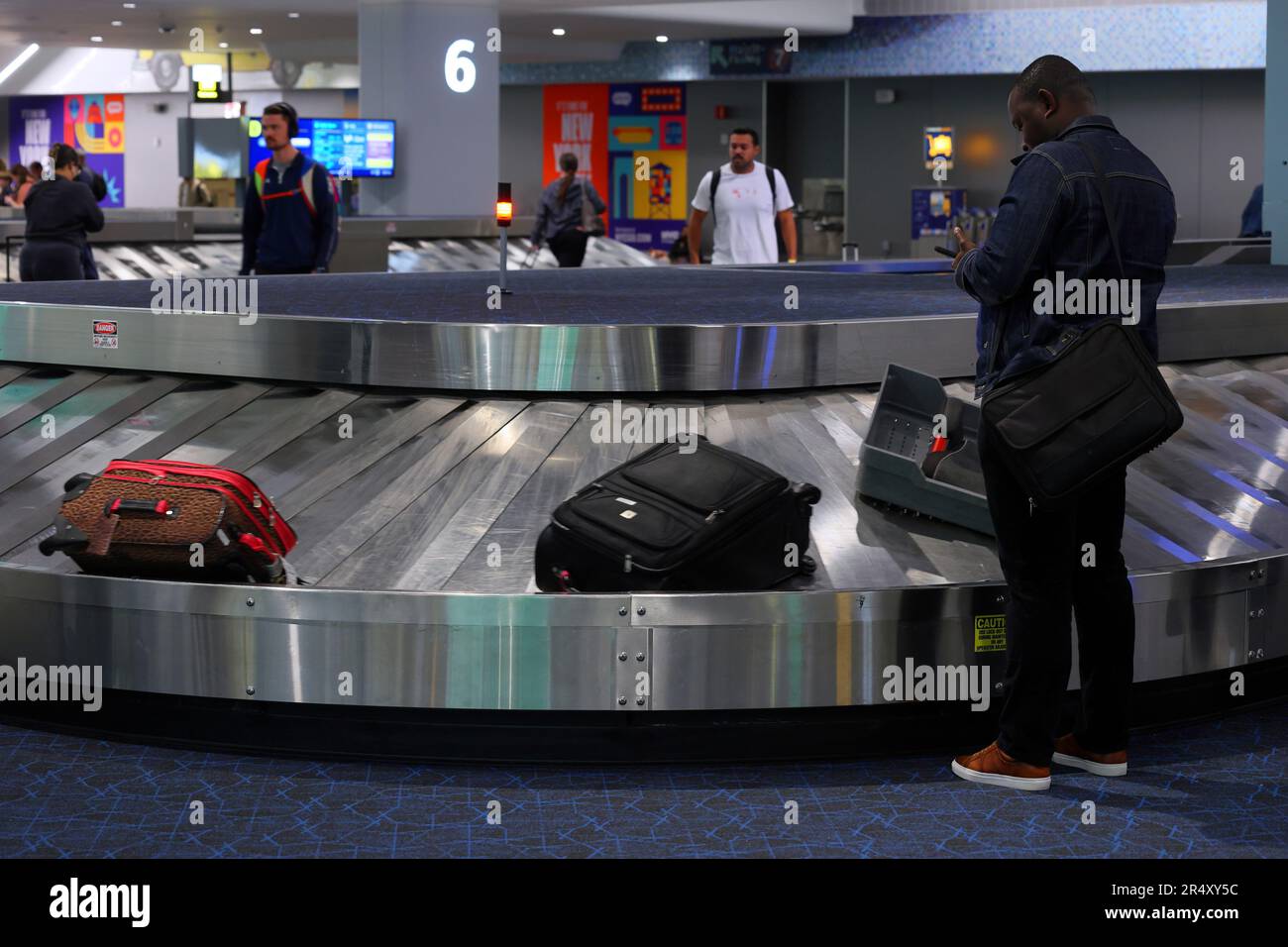 Le persone in attesa di ritirare i bagagli da un nastro trasportatore all'aeroporto LaGuardia, nell'area ritiro bagagli del Terminal B, New York City. Foto Stock