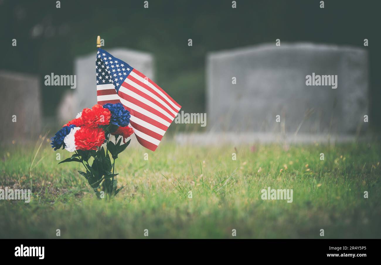 Bandiera americana e fiori rossi, bianchi e blu sulla tomba del veterano. Onorare un soldato caduto nel cimitero il Memorial Day. Foto Stock