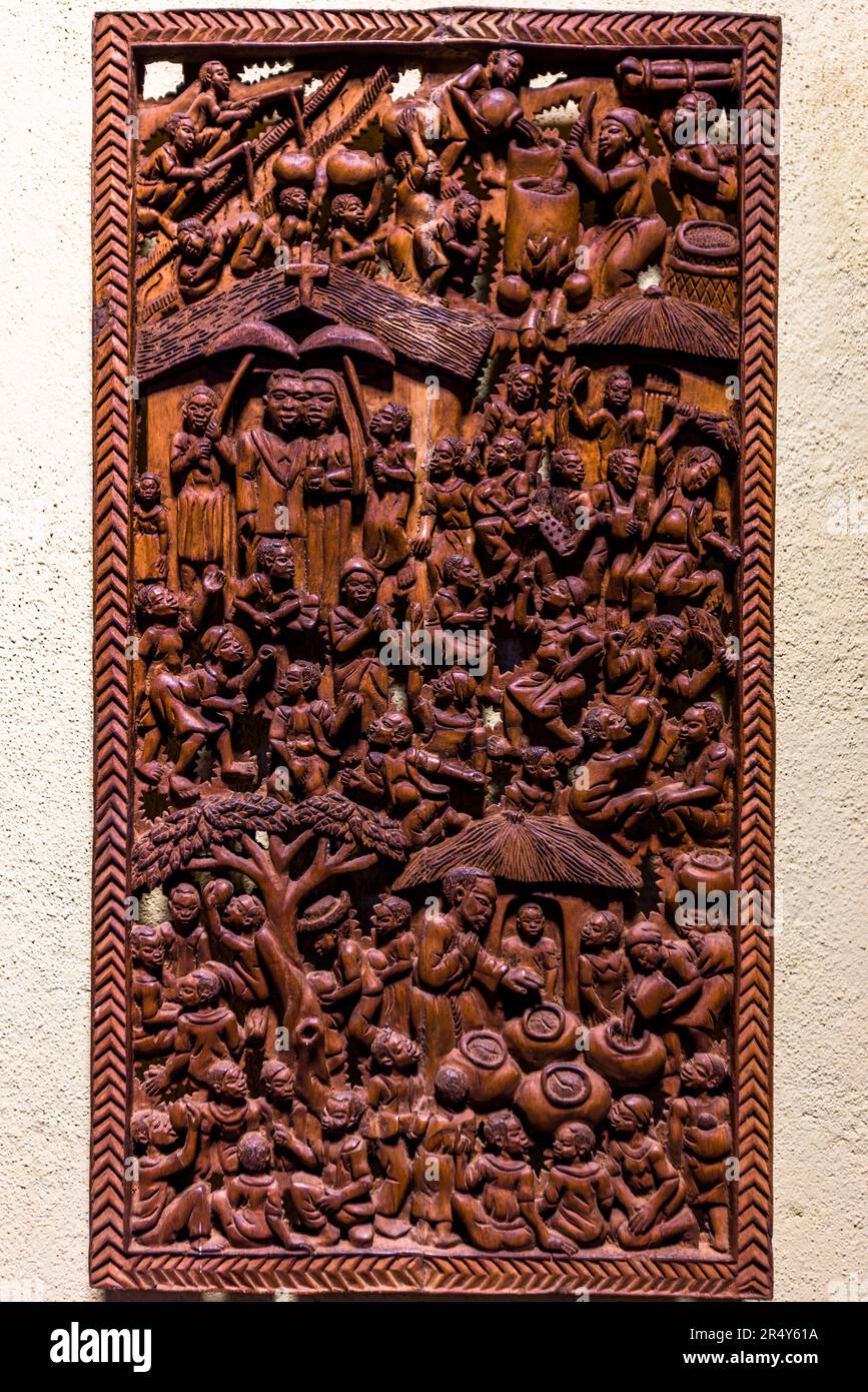 Un pannello di rilievo in legno intagliato raffigura l'arrivo di missionari cristiani in un villaggio africano, circondato da numerose scene della vita quotidiana – esposizione di vendita del Kungoni Centre of Culture and Art a Mua, Dedza, Malawi. Foto Stock