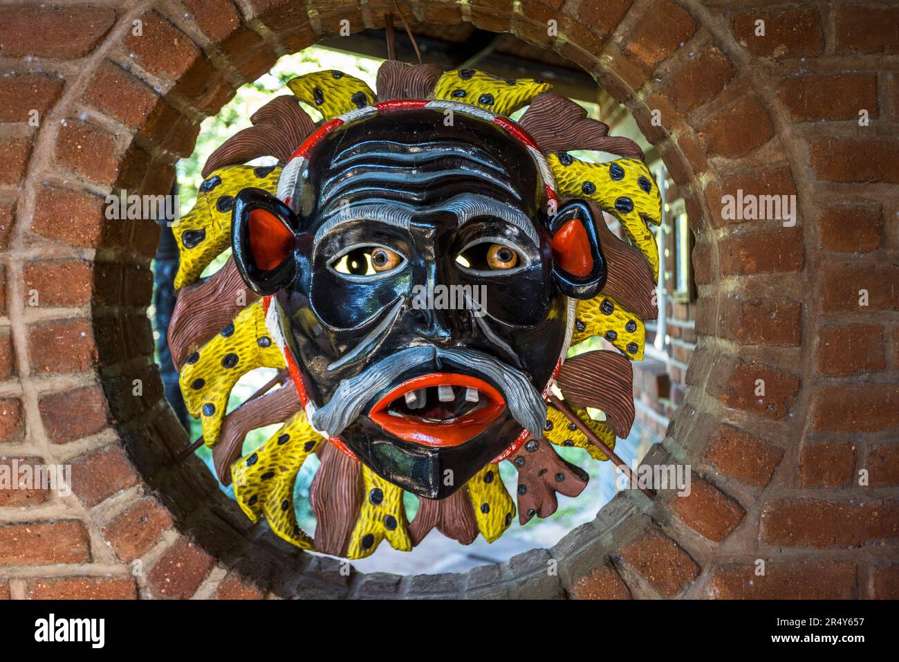 Una maschera Gule Wamkulu dipinta con un collare a motivi giallo e nero è appesa in un'apertura circolare di mattoni al Centro di Cultura e Arte di Kungoni a Mua, Dedza, Malawi. La danza rituale mascherata della società segreta Chewa Nyau è inclusa nella lista del Patrimonio Culturale Immateriale dell'Umanità dell'UNESCO. Foto Stock