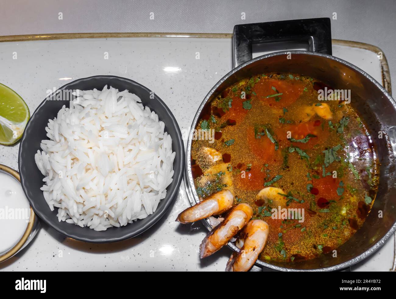Tom Yam, Tom yan, Tom Yum con gamberi, peperoncino, funghi, pomodoro, lime e riso sul lato su un vassoio Foto Stock