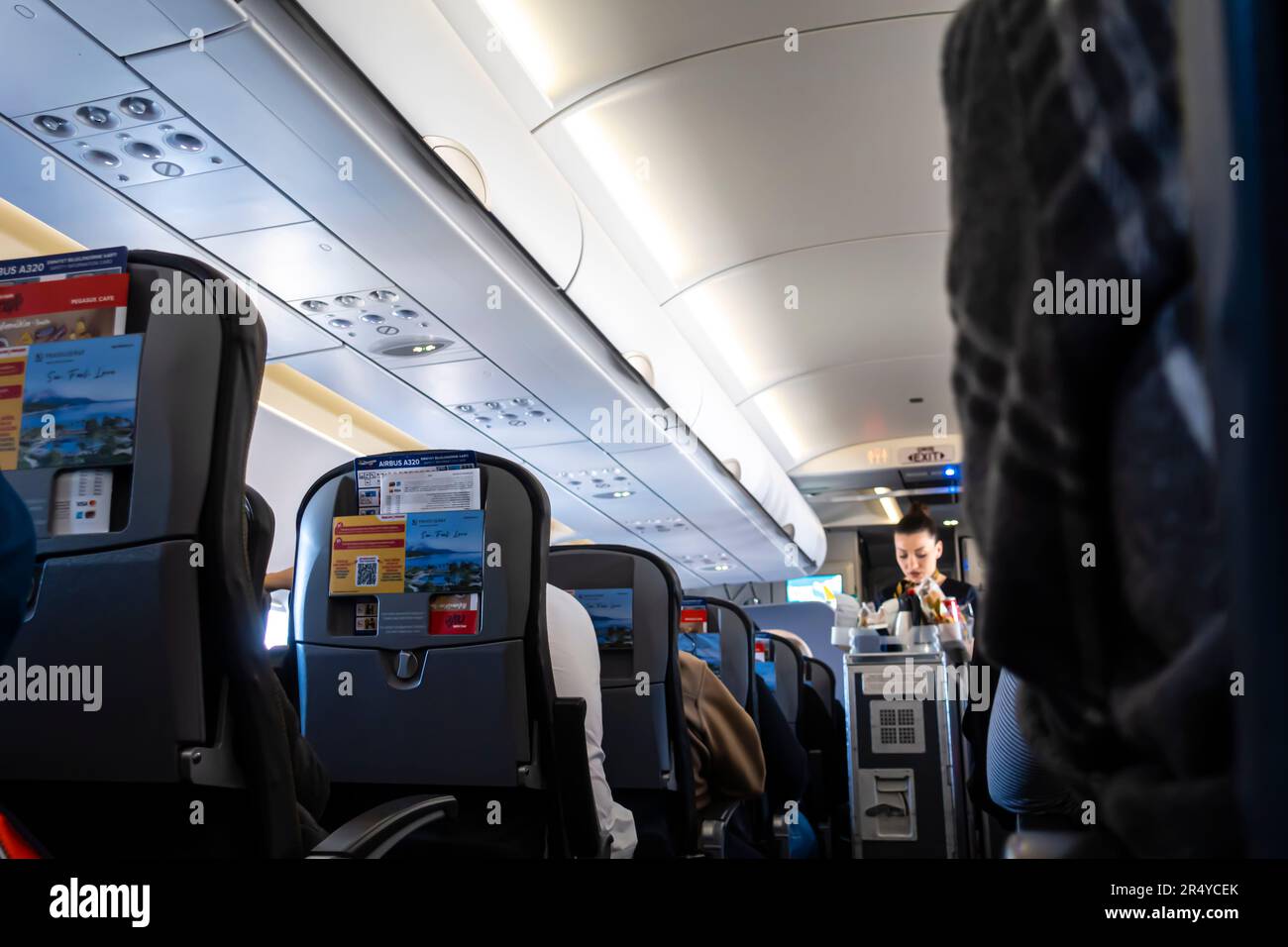 Assistente di volo fuori fuoco, pasto offuscato e bevande serviti ai passeggeri seduti su una sedia in una cabina di aereo Airbus A 320 Foto Stock