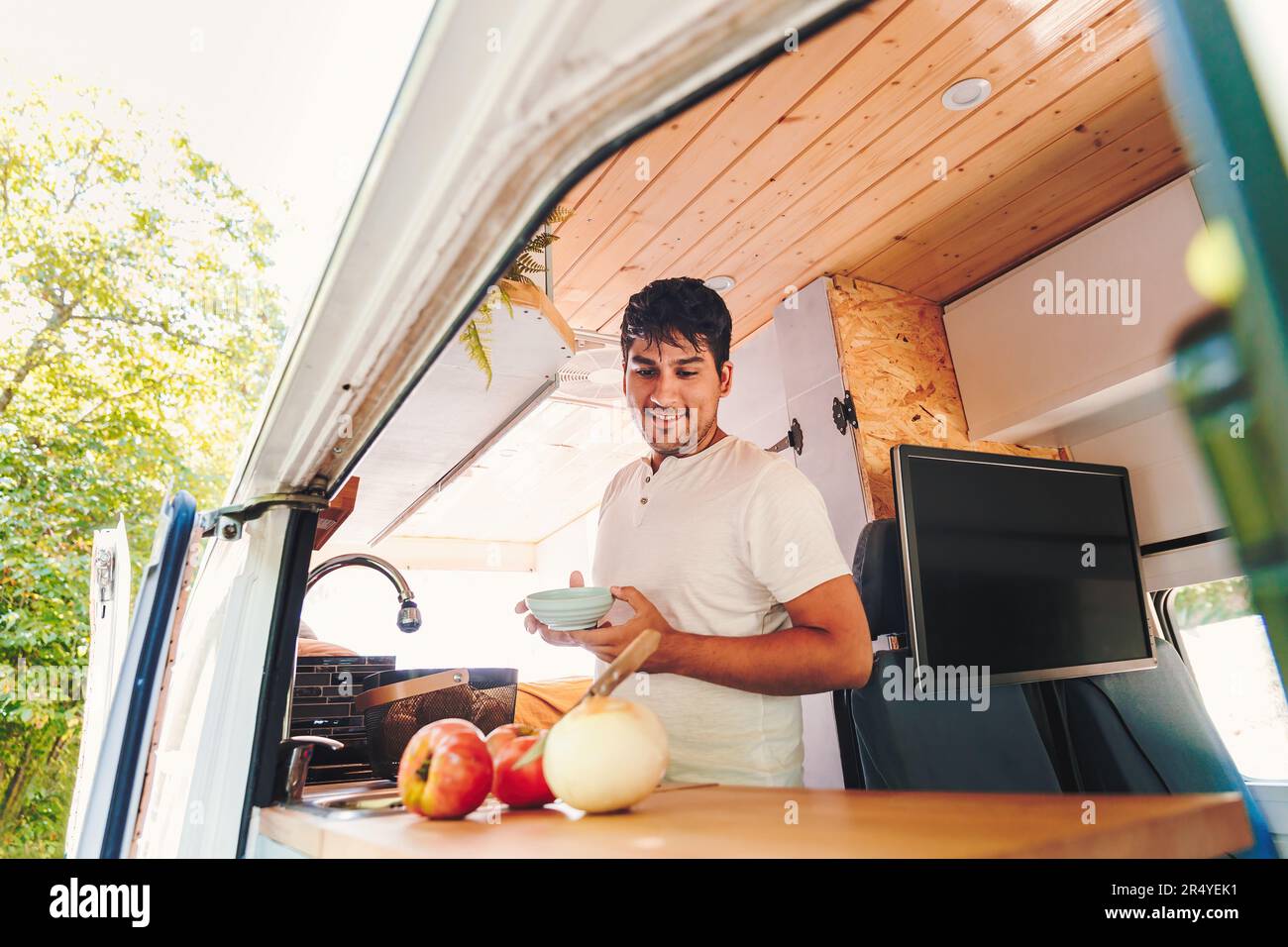 Un uomo ispanico che cucinava il pasto nella cucina del suo camper. Viaggio in pulmino e avventura estiva all'aperto. Concetto di stile di vita Nomad Foto Stock
