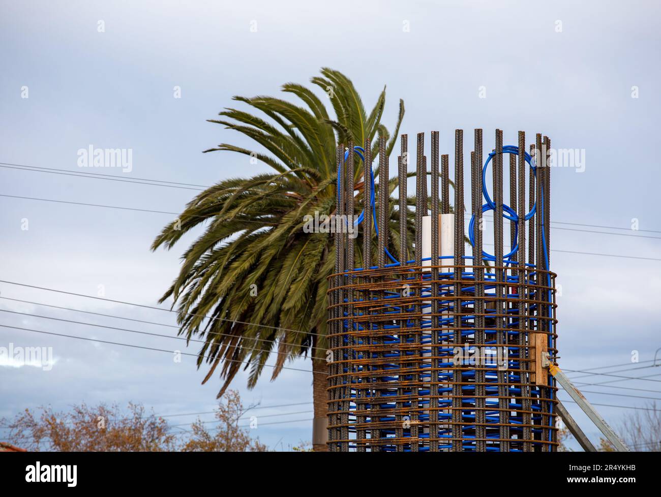 Basamento del ponte ferroviario in costruzione, barre di acciaio di rinforzo unite in un cerchio con tubazioni blu e una palma. Foto Stock