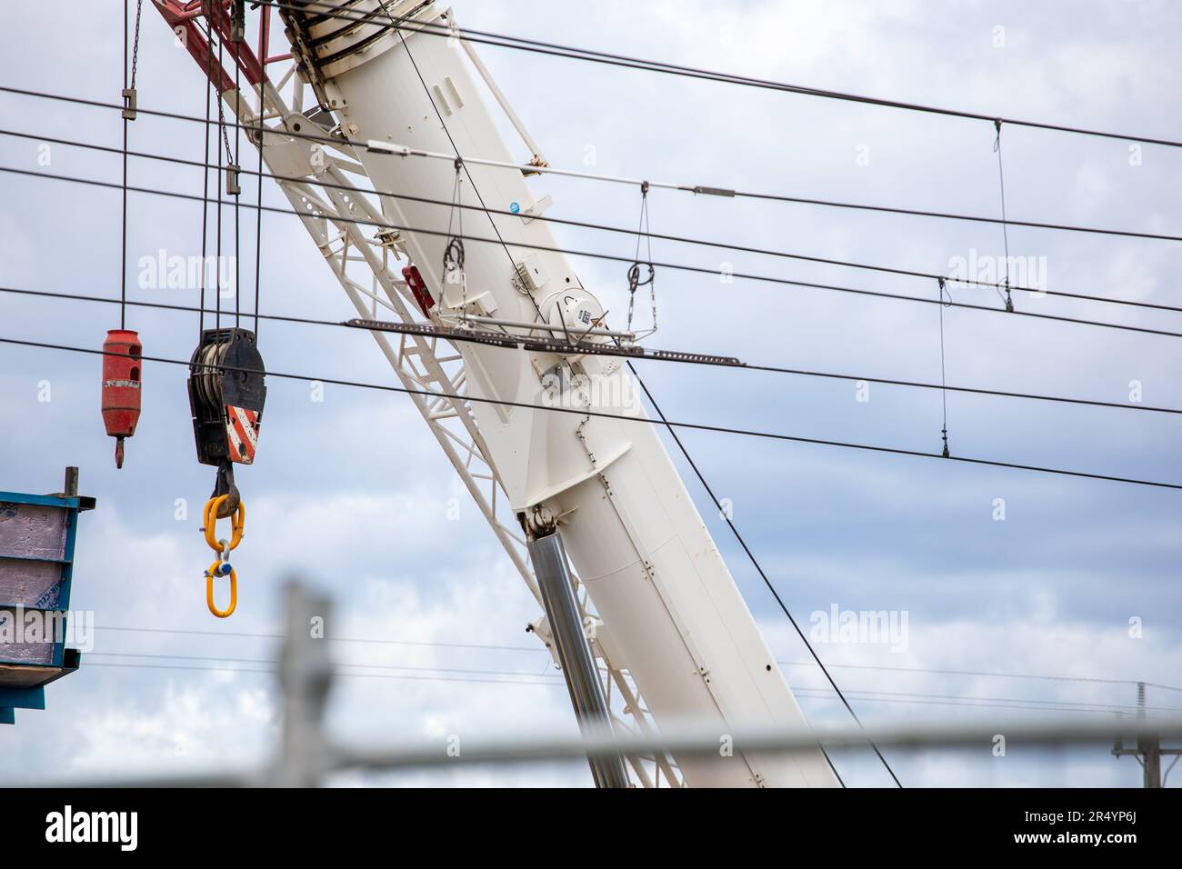 Braccio della gru bianco con ganci gialli e linee di alimentazione del treno. Primo piano contro un cielo grigio. Piccola sezione del ponte ferroviario. Foto Stock