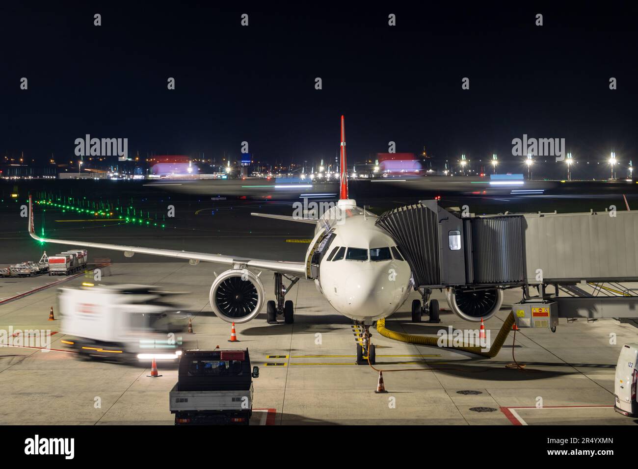 Un aereo si trova sul ponte d'imbarco di notte con un aereo in movimento sullo sfondo Foto Stock