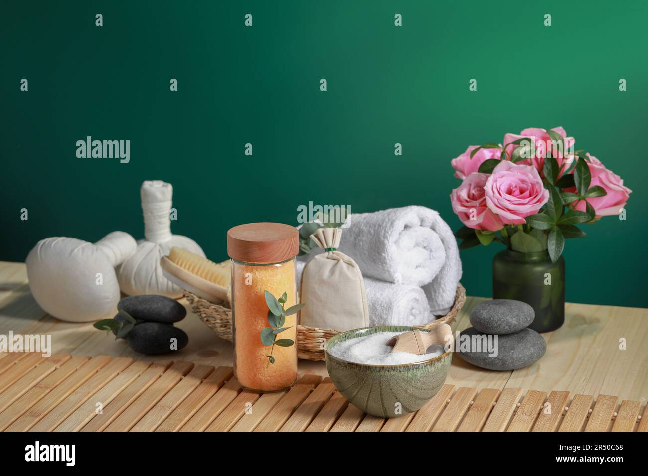Bella composizione con sale marino, fiori e diversi prodotti termali su tavolo di legno vicino parete verde, spazio per il testo Foto Stock