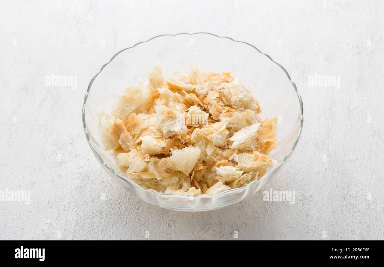 Ciotola di vetro con pezzi di pasta sfoglia per un delizioso dessert arabo umm ali o altro piatto su sfondo grigio chiaro. Fase di cottura Foto Stock