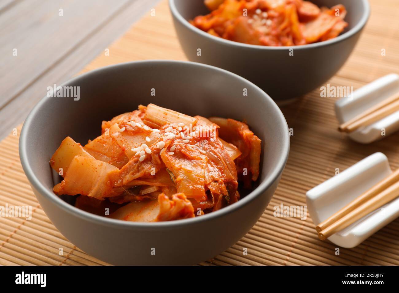 Ciotole di cavolo piccante kimchi e bacchette su tappeto di bambù, primo piano Foto Stock