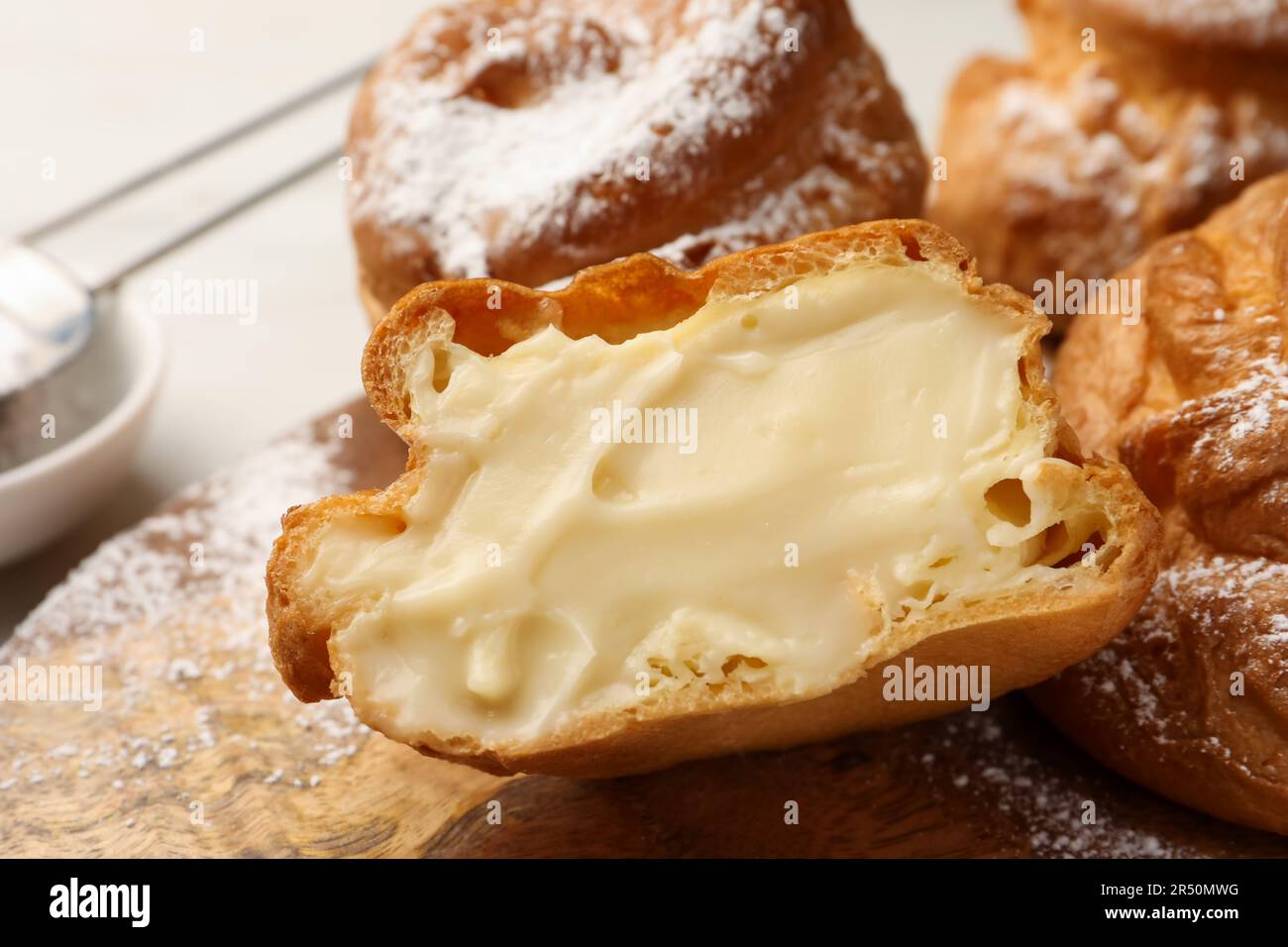 Deliziosi profiteroles con crema ripiena all'interno su tavola di legno, primo piano Foto Stock