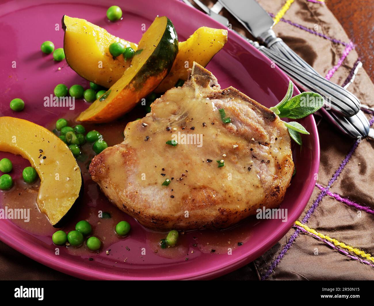 Una trita di maiale con osso in padella fritta con salsa di gocciolamenti in padella, fette di zucca di acorno e piselli Foto Stock