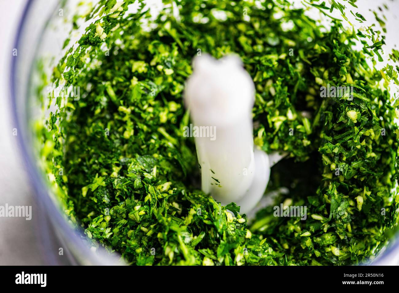 Spinaci freschi crudi e aglio nel recipiente del tritatutto come ingredienti per la cottura del pesto Foto Stock