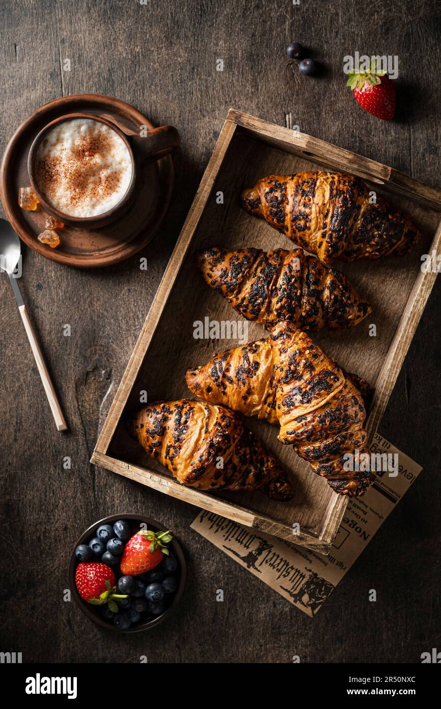 Croissant in un vassoio di legno con una tazza di caffè e frutti di bosco freschi su un tavolo di legno Foto Stock