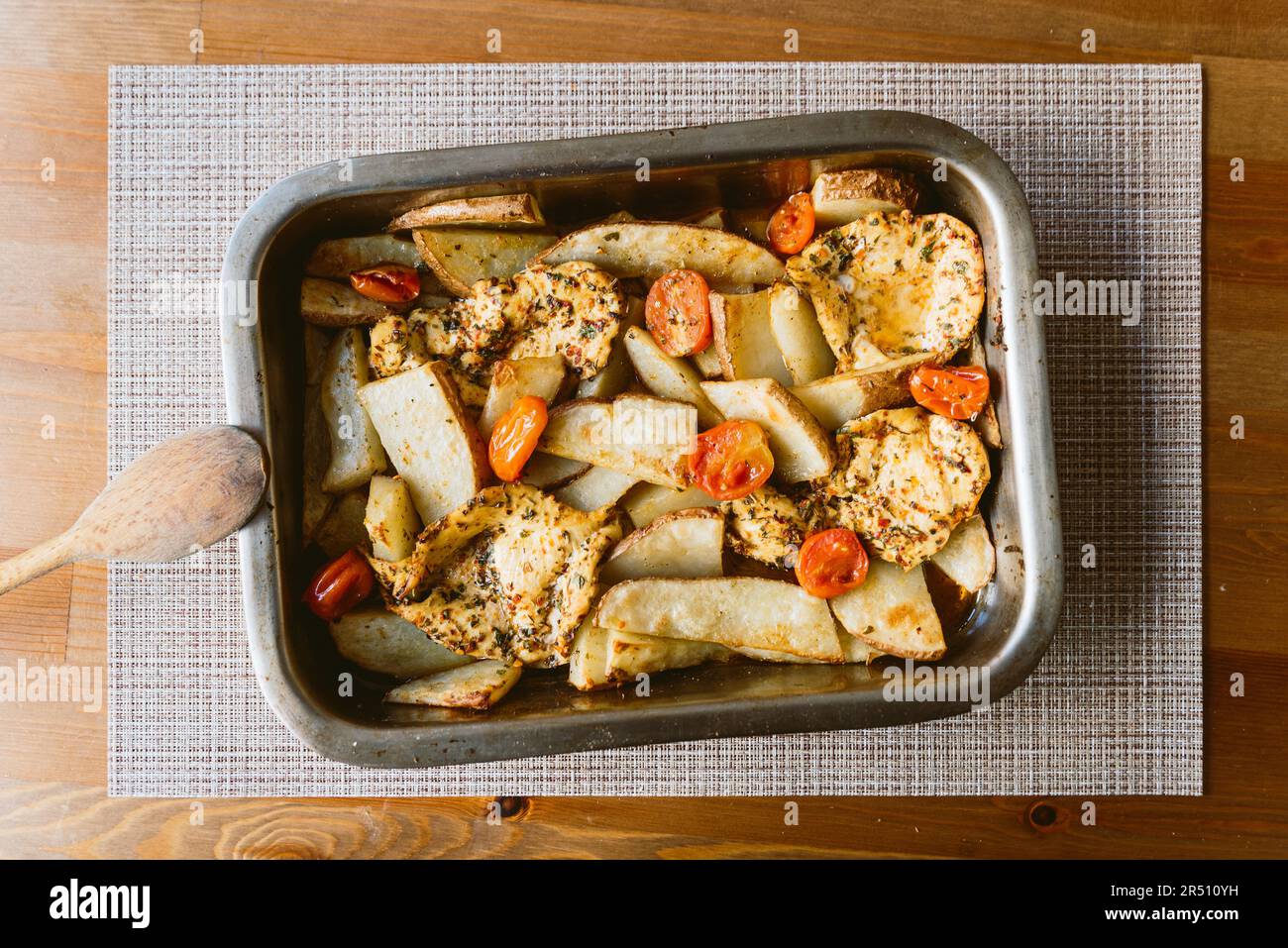 pollo al forno fatto in casa con patate e pomodori su tavolo di legno in vassoio di alluminio. pollo marinato cotto al forno per la tostatura domenicale Foto Stock