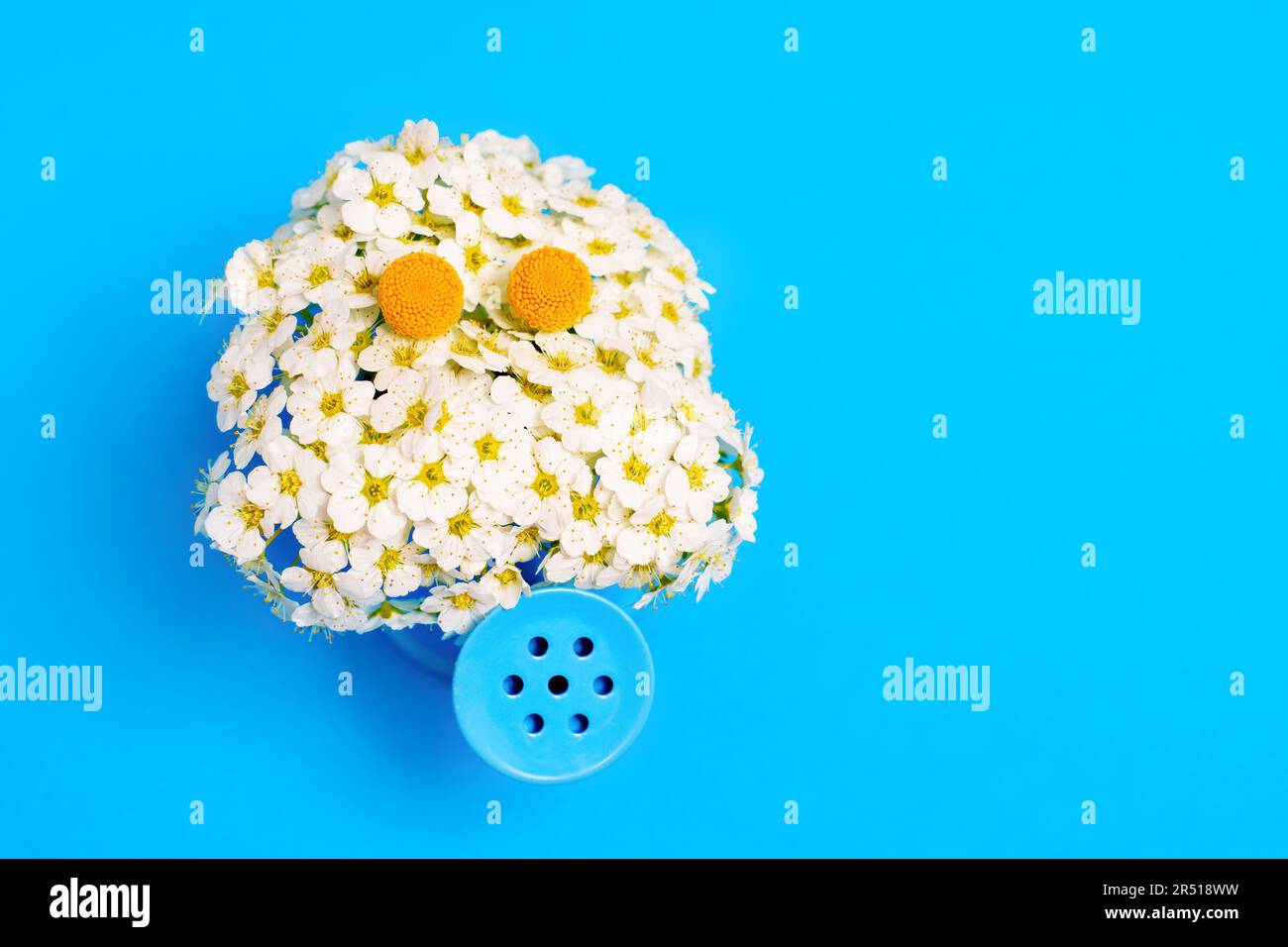 Il carattere delizioso e bizzarro prende vita, realizzato con un lussureggiante bouquet di fiori d'albero e una lattina da annaffiatura in miniatura, sullo sfondo di un blu vibrante Foto Stock