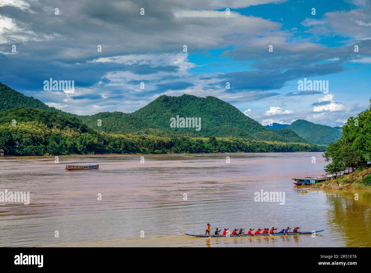 Una tradizionale barca lenta del Laos scivola attraverso il fangoso bacino inferiore del fiume Mekong, circondato da una lussureggiante giungla tropicale e dalla serenità post-pioggia. Foto Stock