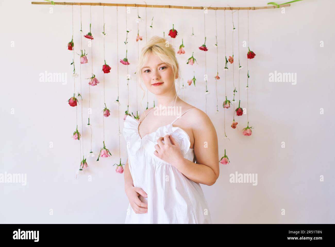 Studio ritratto di bella giovane adolescente 15 - 16 anni ragazza vestito estivo, posa su sfondo bianco con fiori appesi, bellezza e moda Foto Stock