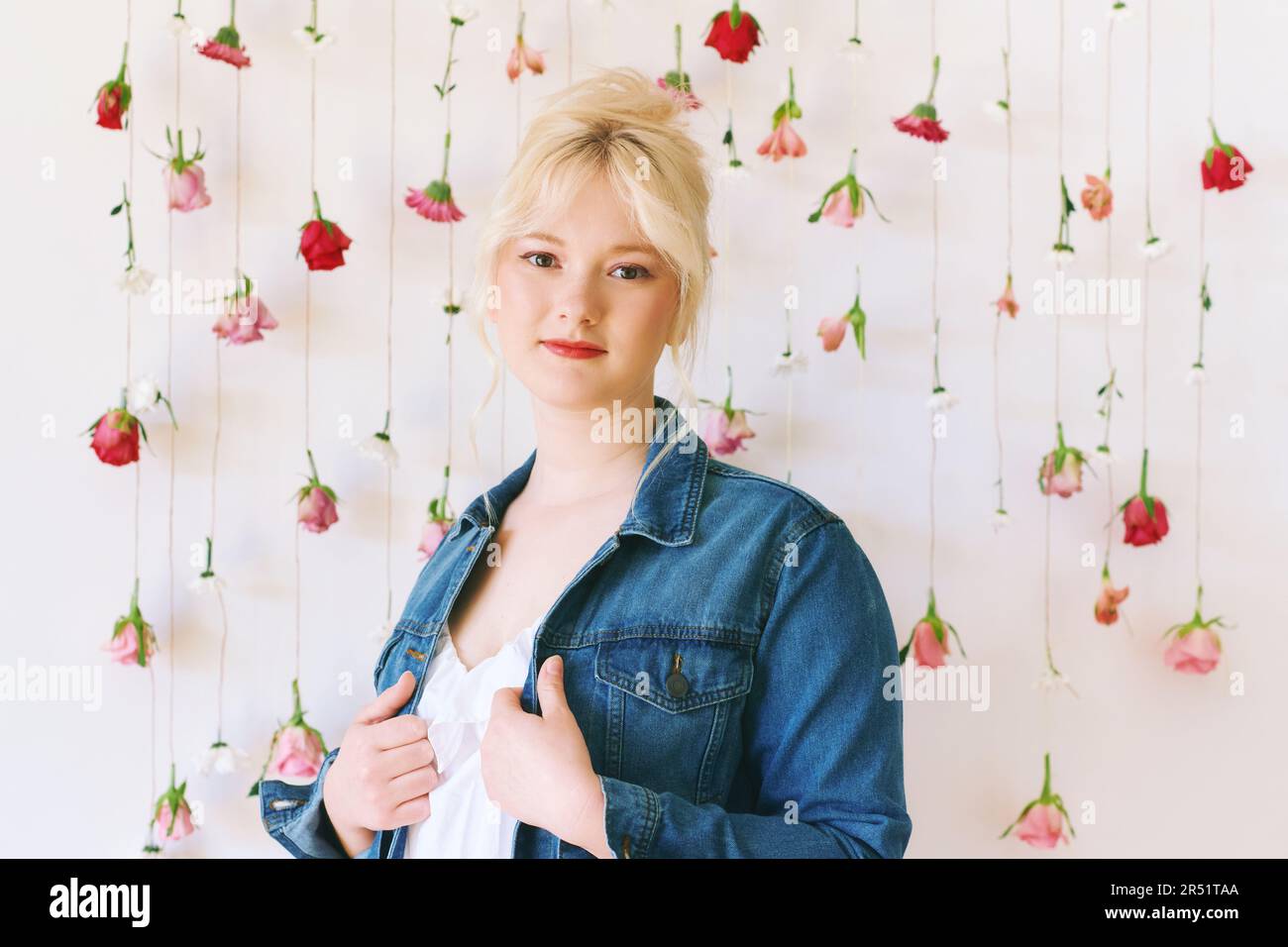 Studio ritratto di bella giovane adolescente 15 - 16 anni ragazza indossa giacca denim, posa su sfondo bianco con fiori appesi, bellezza e moda Foto Stock