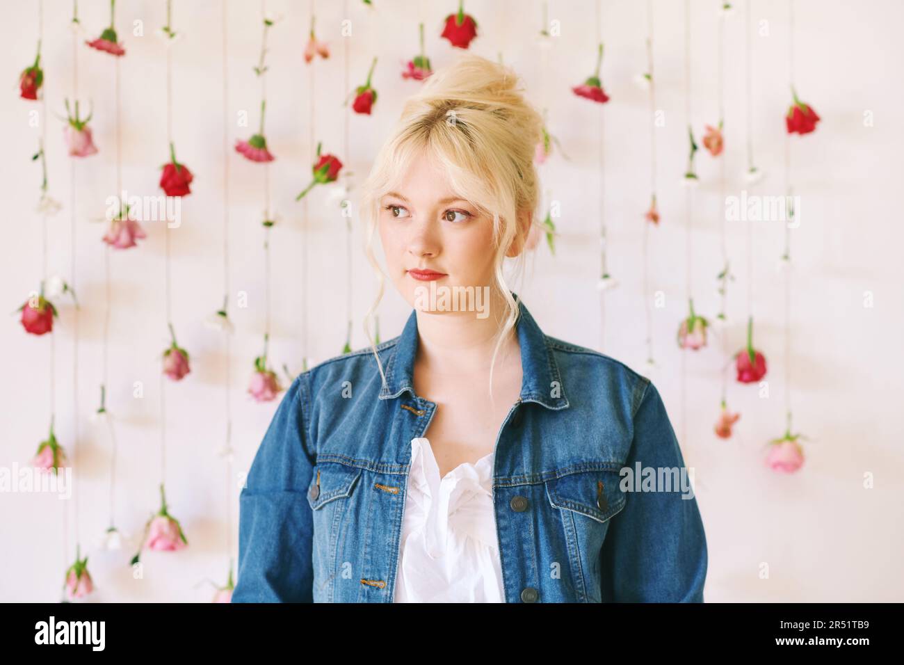 Studio ritratto di bella giovane adolescente 15 - 16 anni ragazza indossa giacca denim, posa su sfondo bianco con fiori appesi, bellezza e moda Foto Stock