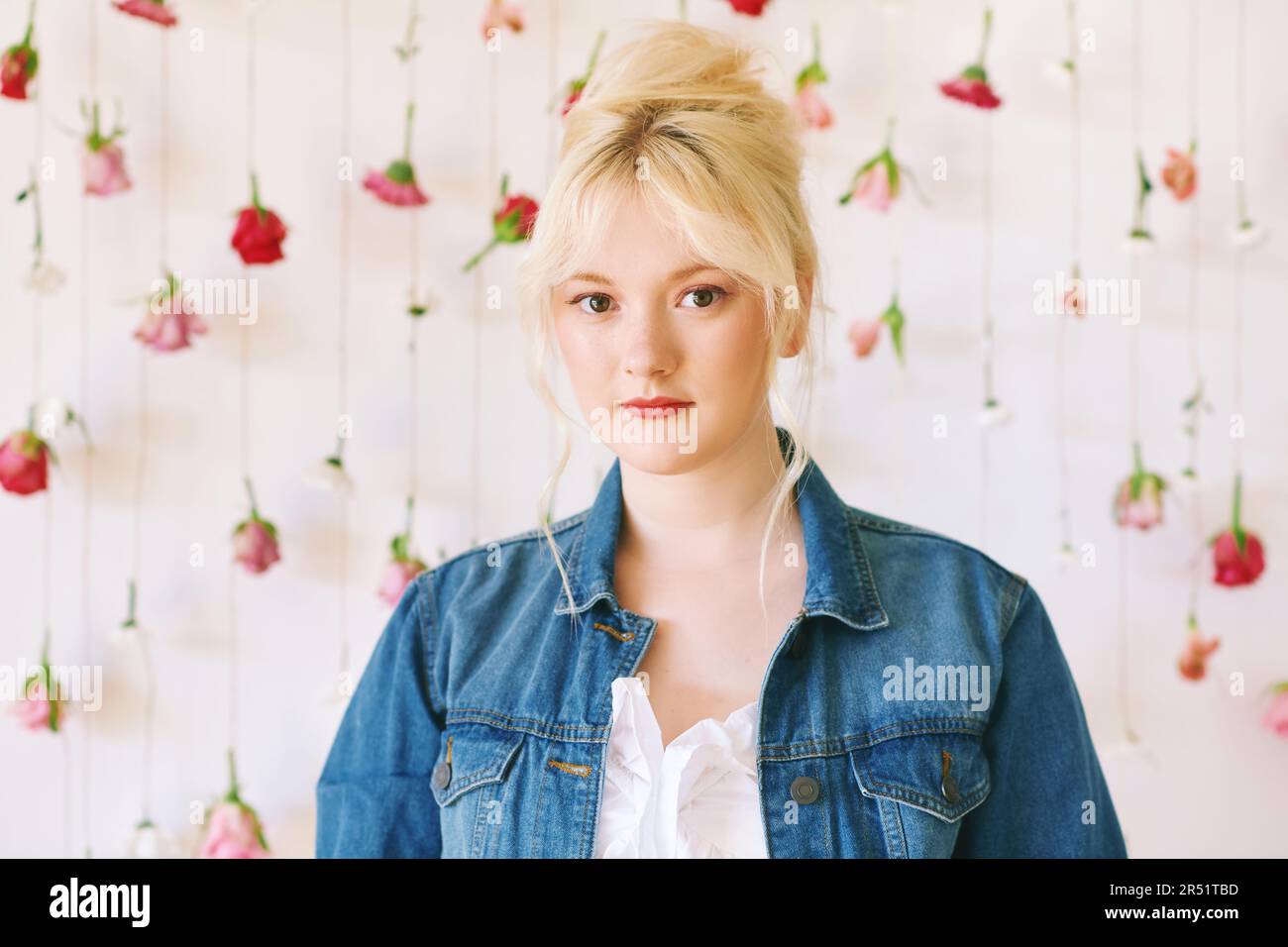 Studio ritratto di bella giovane adolescente 15 - 16 anni ragazza indossa giacca denim, posa su sfondo bianco con fiori appesi, bellezza e moda Foto Stock