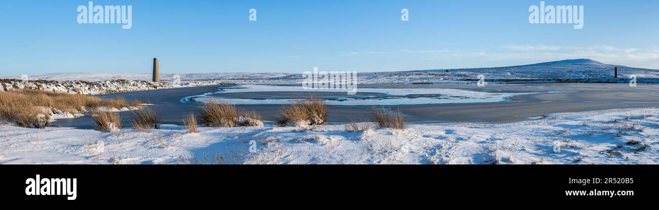 Diga Sikehead, bacino idrico e vecchi camini di canna fumaria industriale sulla brughiera della contea di Durham in inverno con erba, neve e ombre basse del sole in primo piano Foto Stock