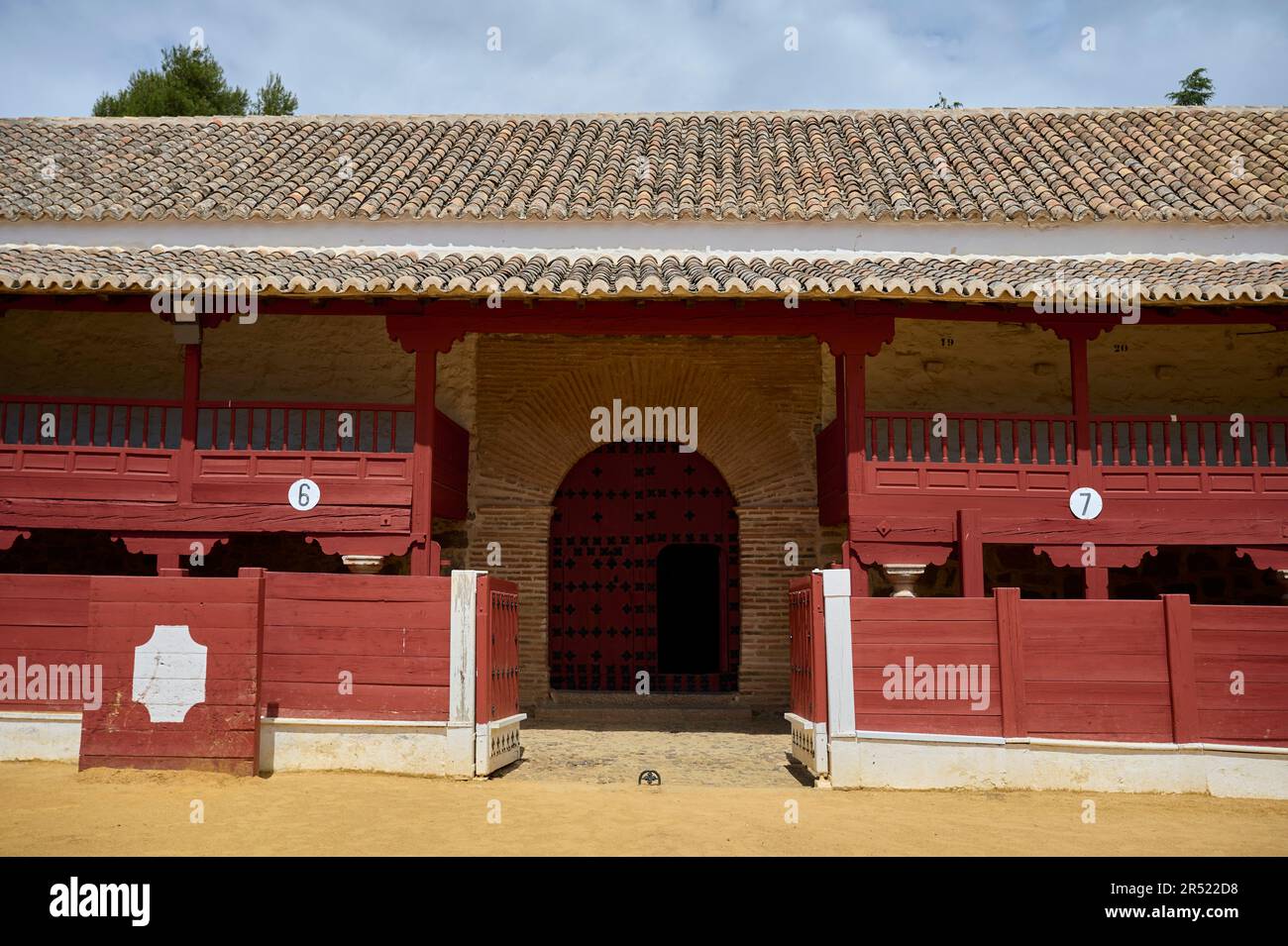 Vecchio edificio di bullring con tetto piastrellato e porta ad arco sotto cielo nuvoloso blu, mentre fornito di numeri contrassegnati rosso spettatore gallerie Foto Stock