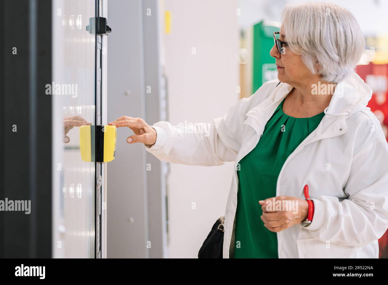 Donna anziana in bicchieri e abiti casual scegliendo le merci in moderno frigorifero nel terminal dell'aeroporto in attesa di partenza Foto Stock