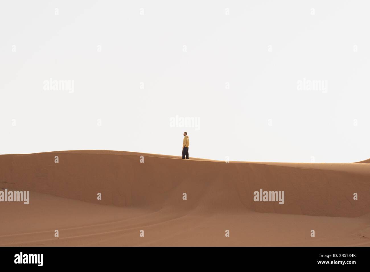 Vista laterale di una persona distante che cammina su dune sabbiose contro il cielo nuvoloso della città di Marrakech durante il viaggio estivo attraverso il Marocco Foto Stock