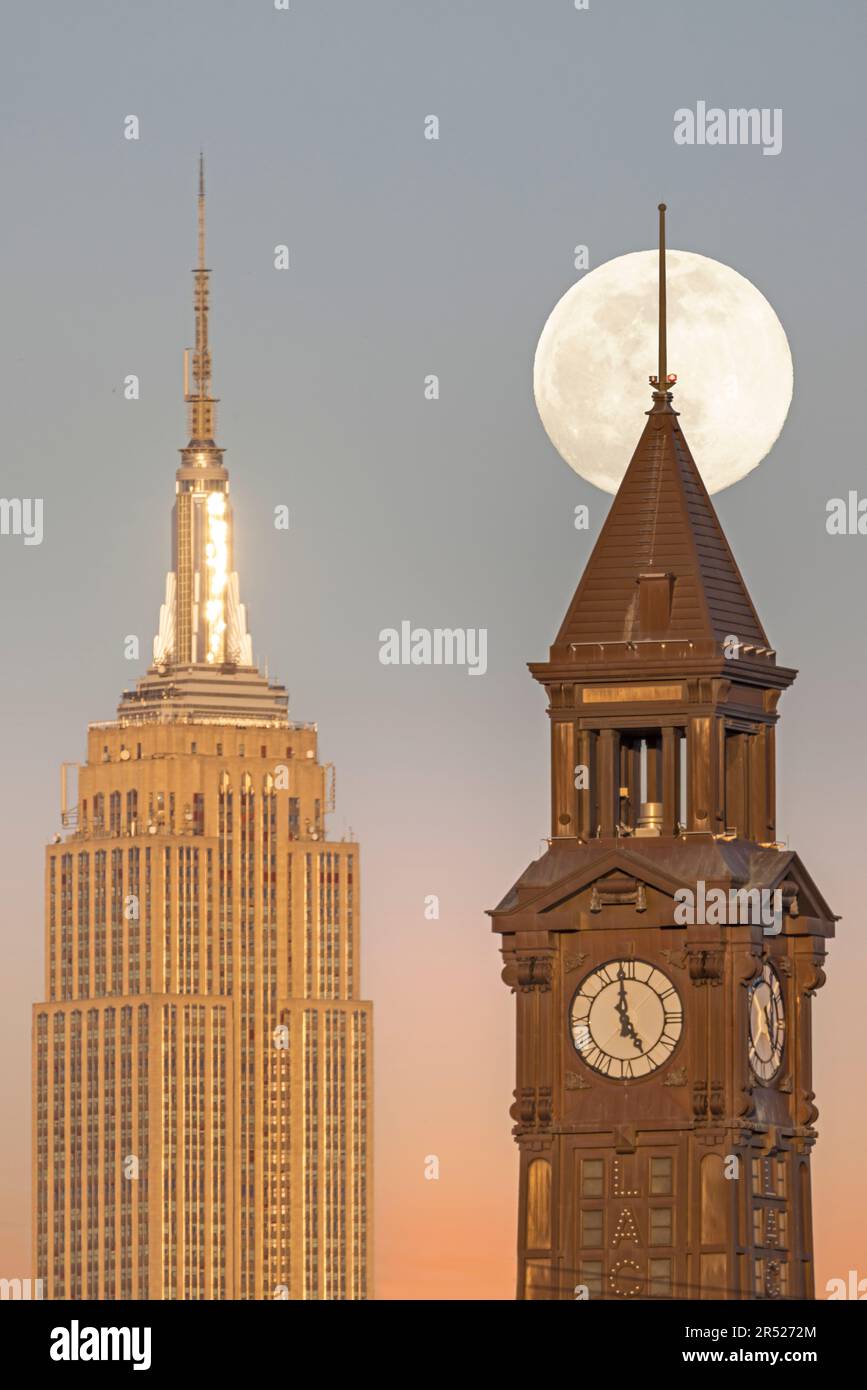 La luna piena sorge dietro la Torre dell'Orologio di Lackawanna a Hoboken, New Jersey, accanto all'iconico Empire state Building e al 1 Vanderbilt Foto Stock