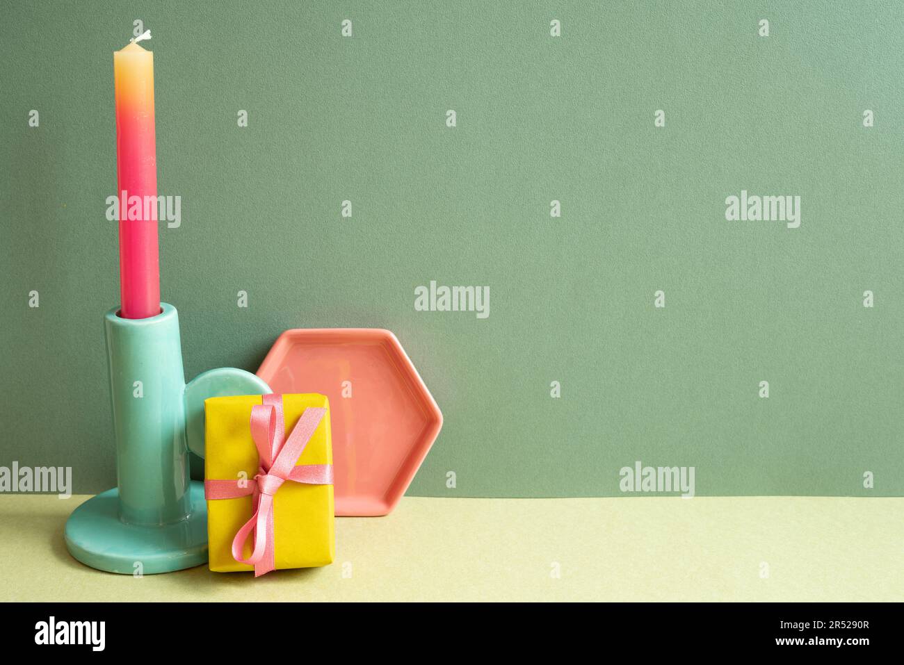 Confezione regalo gialla, candela rosa e supporto sul tavolo. sfondo parete verde Foto Stock