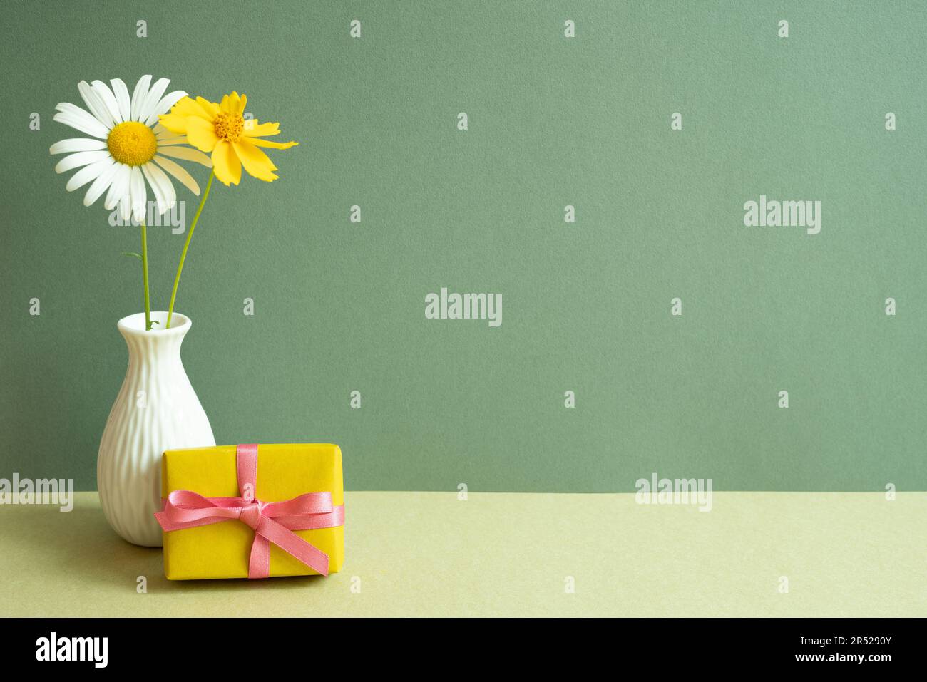 Scatola regalo gialla, vaso di fiori su tavolo. sfondo parete verde. spazio di copia Foto Stock