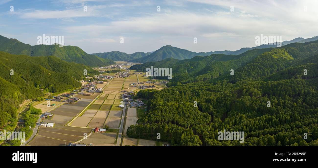 Lussureggianti montagne verdi circondano campi di riso e piccolo villaggio agricolo Foto Stock