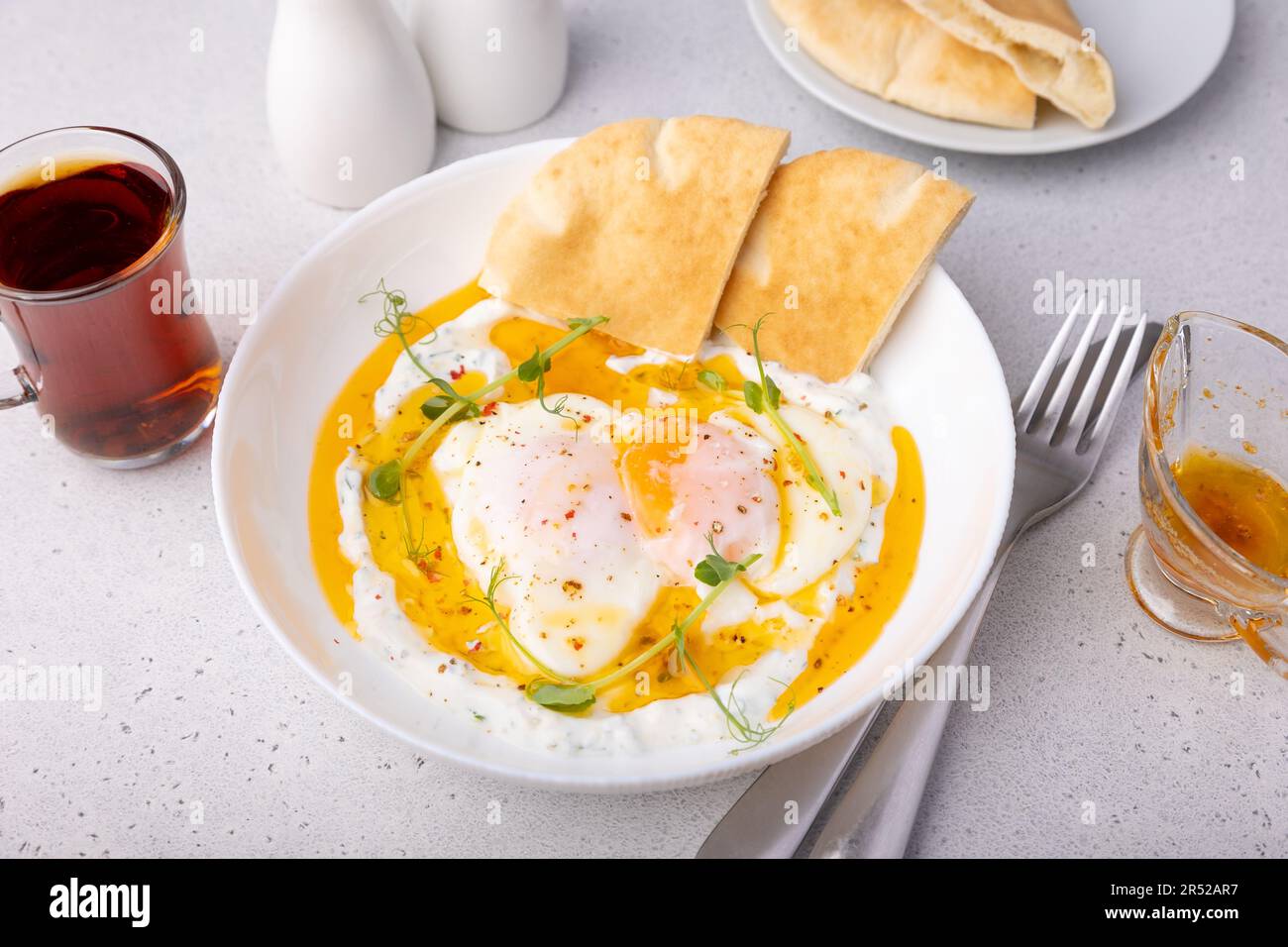 Uova turche (chilbir) con yogurt, burro profumato, arachidi di piselli, pane piatto e tè. Tradizionale colazione turca con uova in camicia (con tuorlo liquido Foto Stock