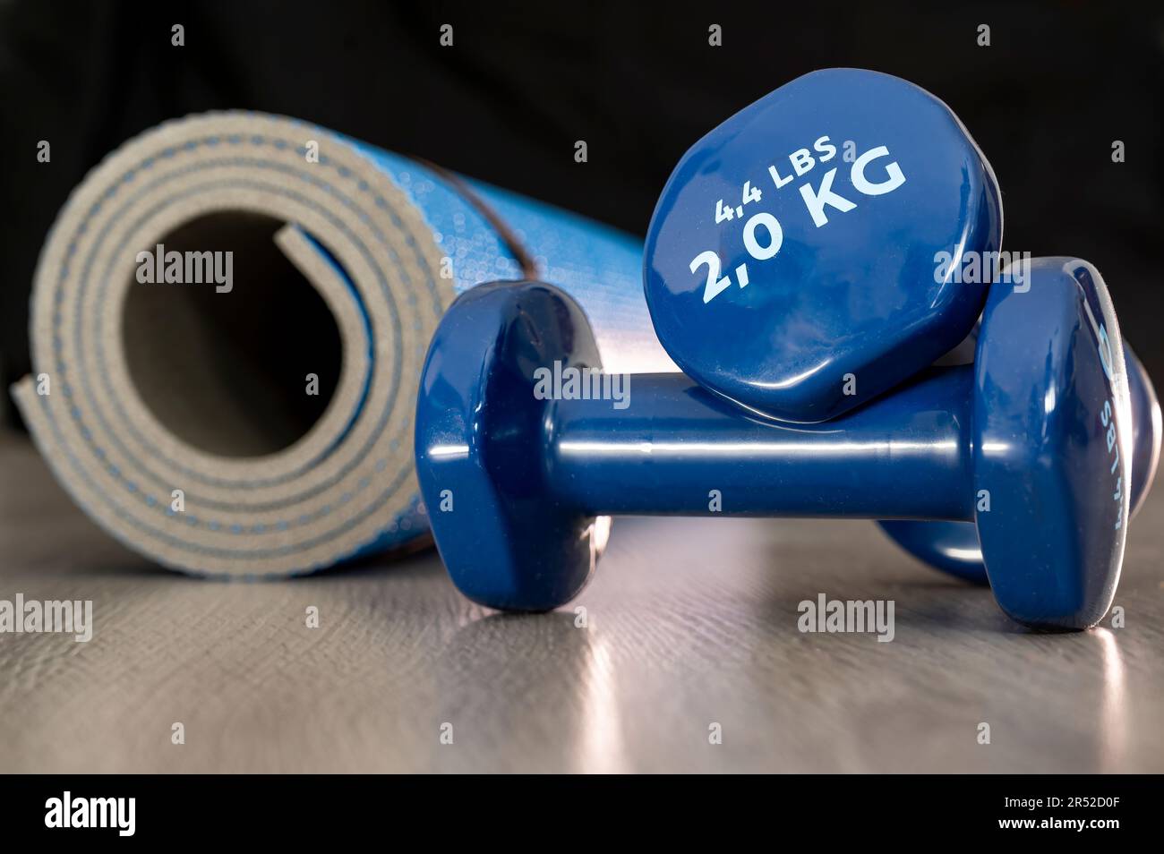 Piccoli manubri in vinile blu usati per yoga, pilates e altri sport vicino a un tappeto arrotolato Foto Stock