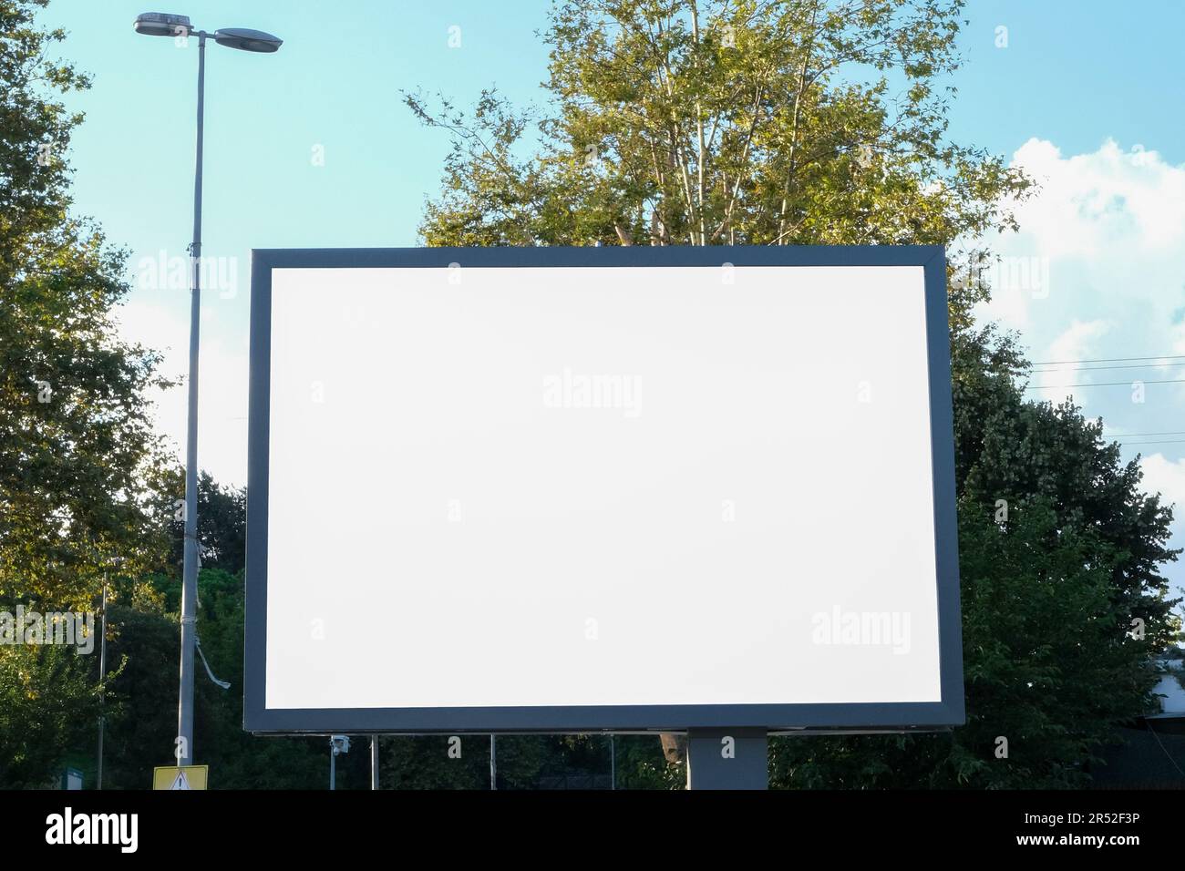 Bianco pubblicità cartello mostra tabellone mockup fuori con alberi e cielo blu nuvoloso sfondo. Sfondo bianco banner cartellone in città. Foto Stock