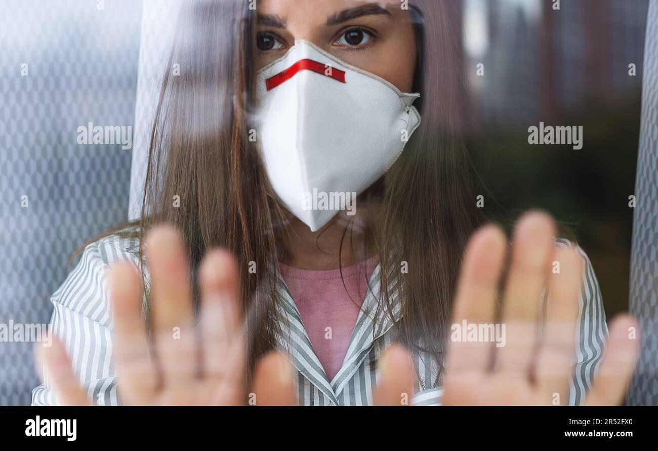 Giovane donna in maschera medica rimanere isolamento a casa per auto quarantena. Concetto di quarantena domestica, prevenzione COVID-19, situazione di focolaio di Coronavirus Foto Stock