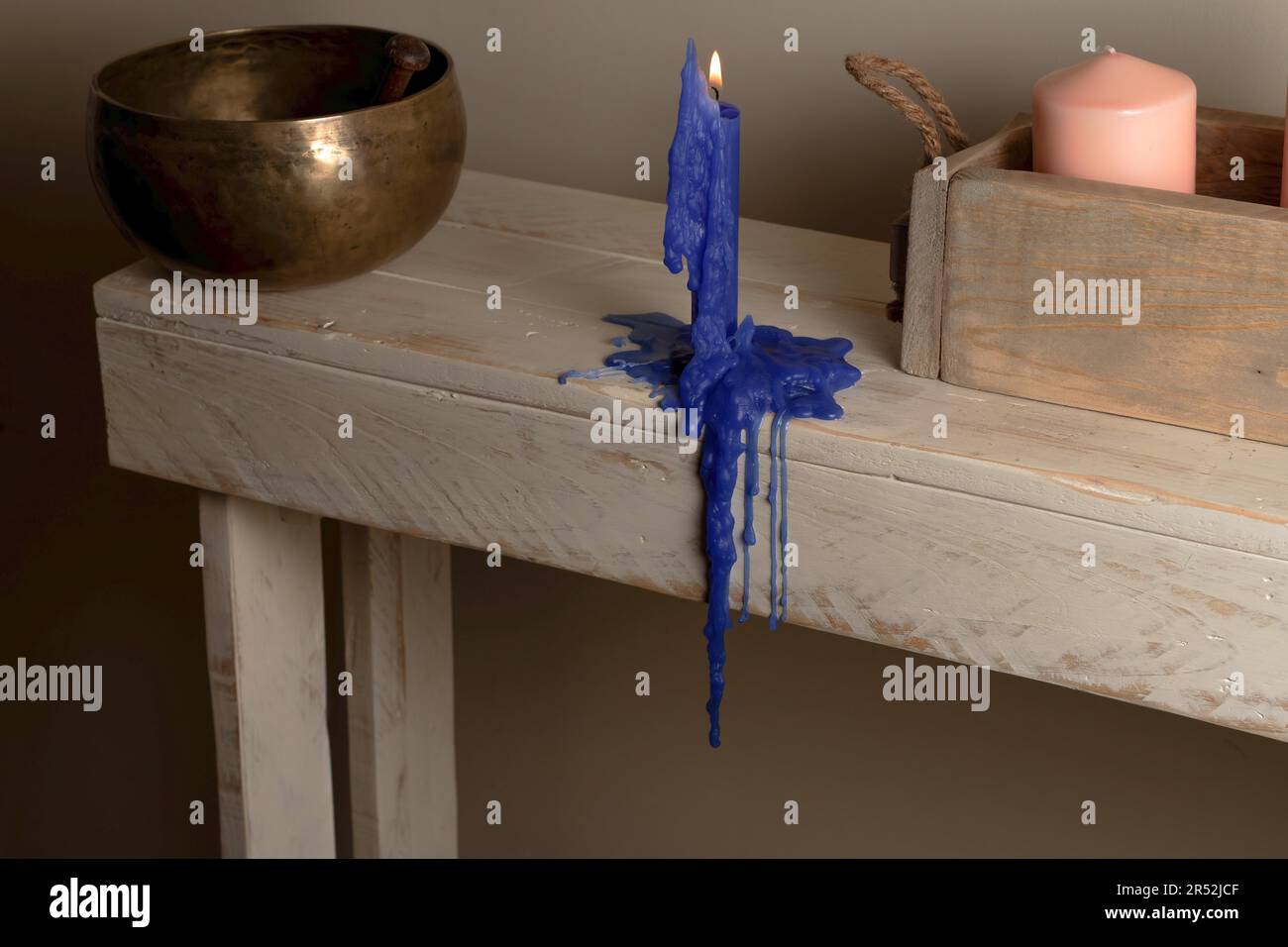 Candela blu illuminata fusa su un tavolo di legno con una ciotola tibetana sullo sfondo e una scatola di legno con una candela rosa Foto Stock