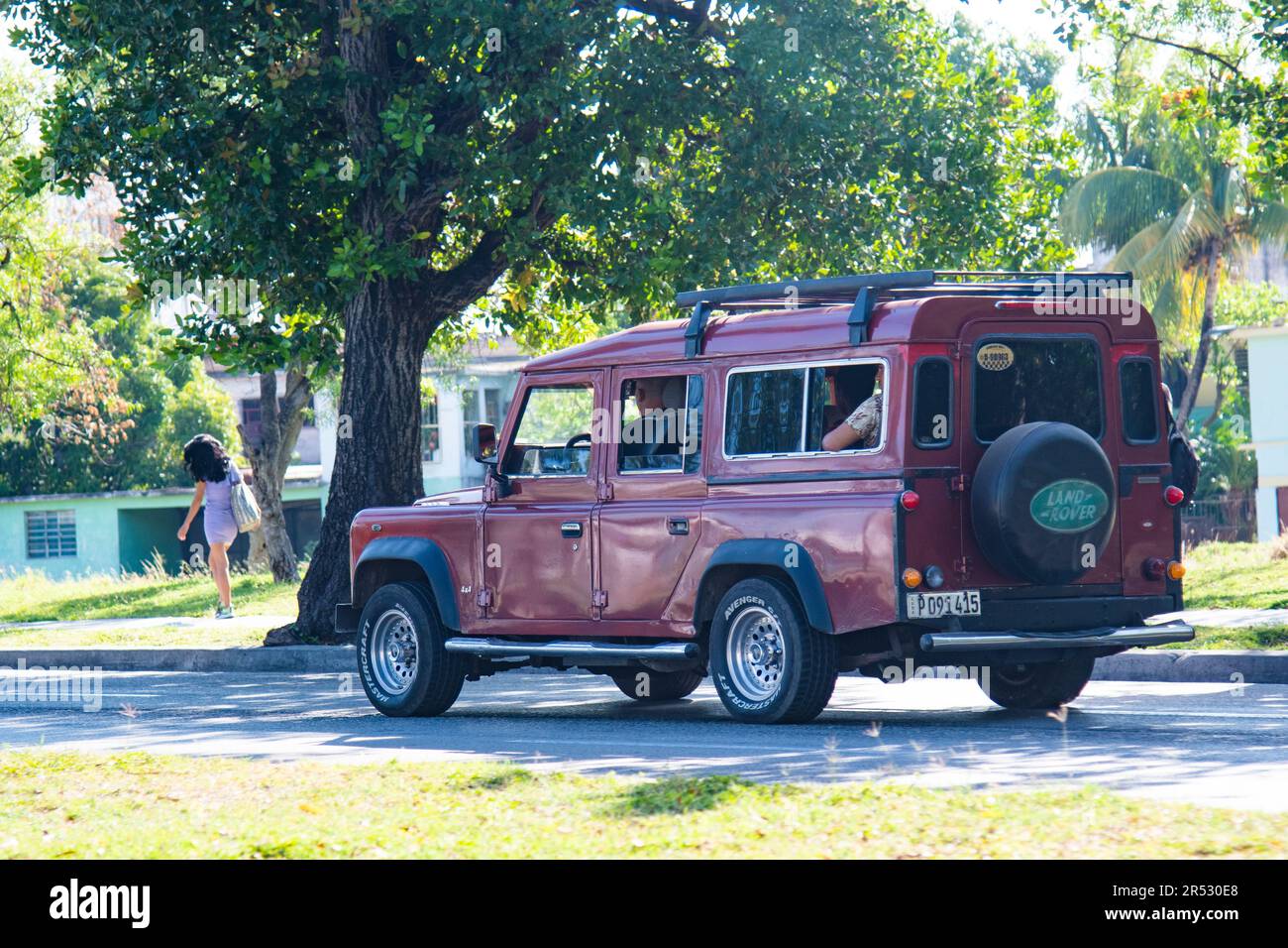 La vecchia macchina cubana rossa guida lungo una strada a l'Avana, Cuba, con un pneumatico Land Rover sul retro del veicolo. Foto Stock
