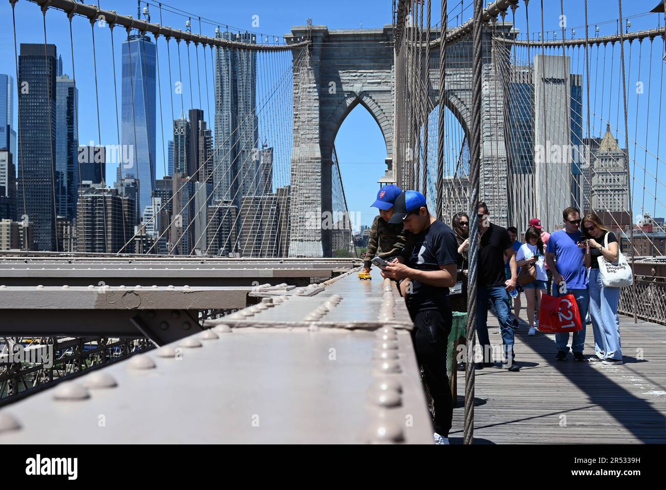 I visitatori si trovano sulla passerella pedonale del Ponte di Brooklyn con lo skyline di Manhattan sullo sfondo. Foto Stock