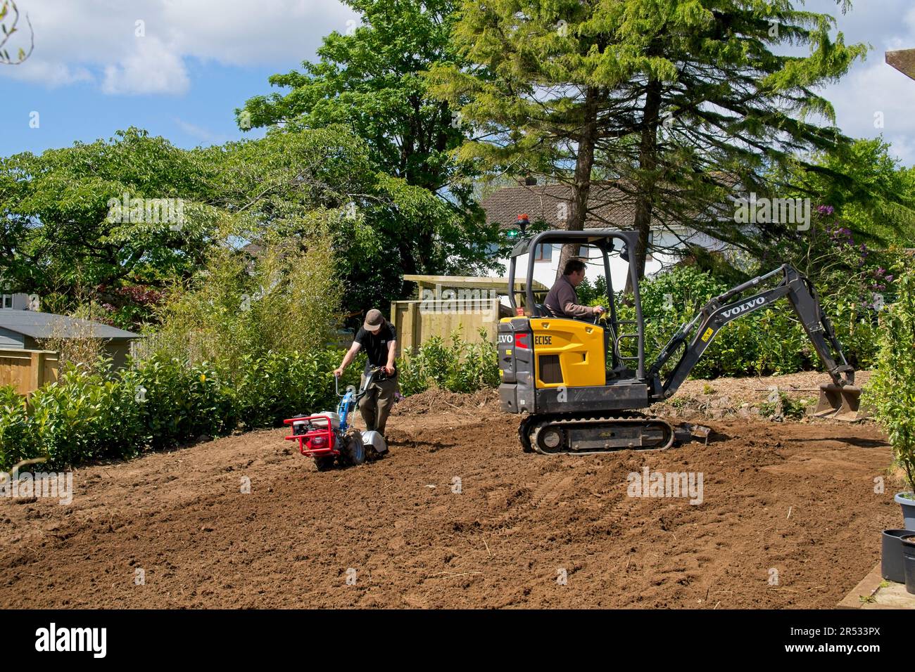 Gower Wales UK maggio 2023 macchinario preparatore terreno per prato di ricambio. Escavatore meccanico e rotavator in uso. Alberi e cespugli sullo sfondo. Foto Stock