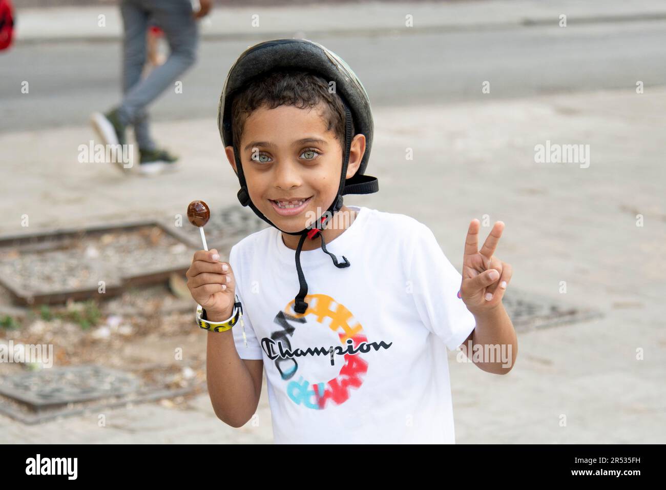 Un giovane ragazzo cubano con occhi incredibili sorride e dà un segno mentre tiene un papsiclo in una mano alla macchina fotografica a l'Avana, Cuba. Foto Stock