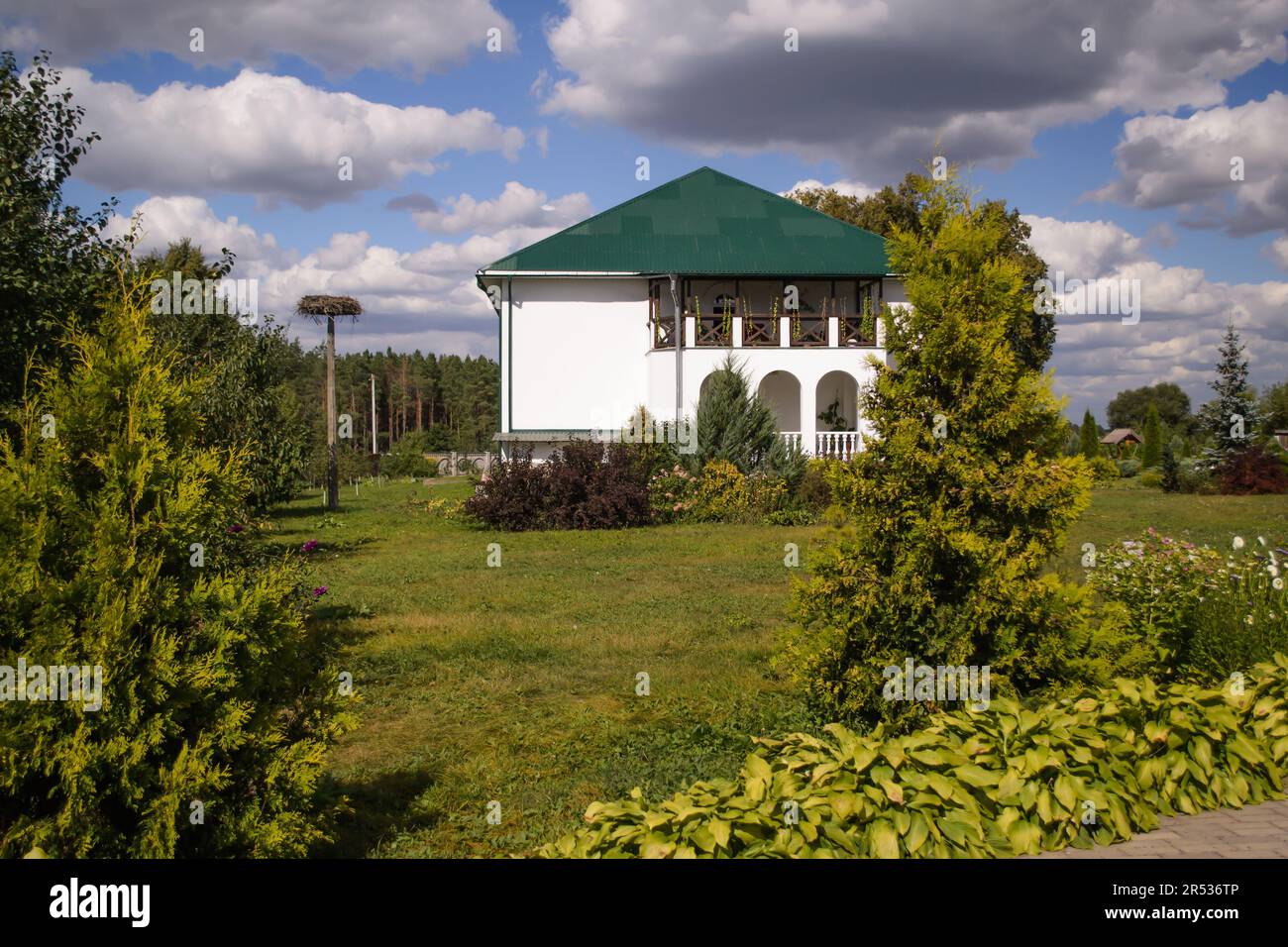 Celle monastiche, in un giardino di conifere, un edificio bianco refettorio, un nido di cicogna sulla sinistra, un vecchio pozzo sulla destra.Foresta sull'orizzonte blu del cielo Foto Stock