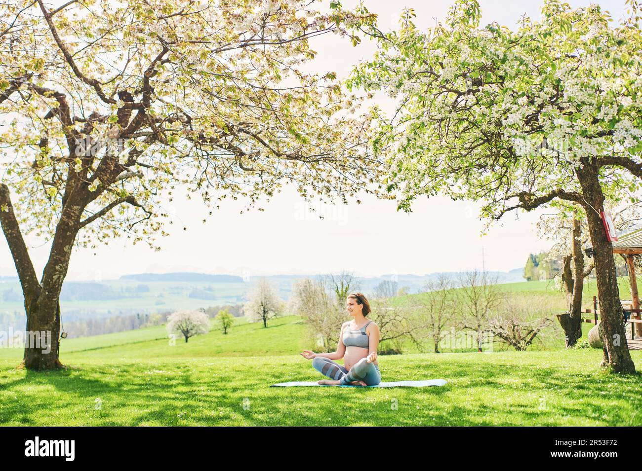 Ritratto all'aperto di felice giovane donna incinta che pratica yooga nel giardino di primavera sotto alberi di mela fiorente, stile di vita sano Foto Stock
