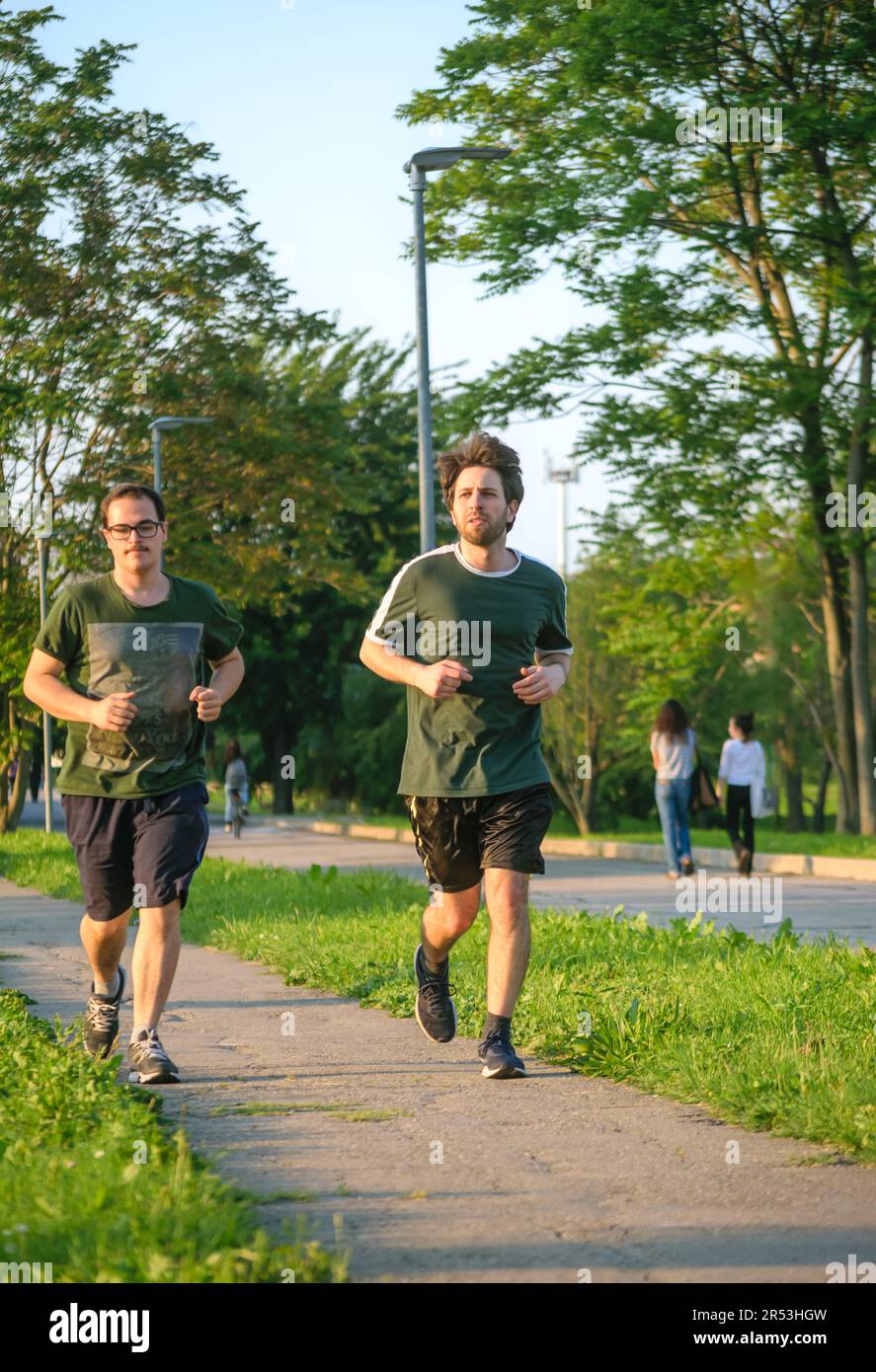 Due amici maschili che corrono con la t-shirt verde allenandosi nel parco nelle giornate di sole Foto Stock