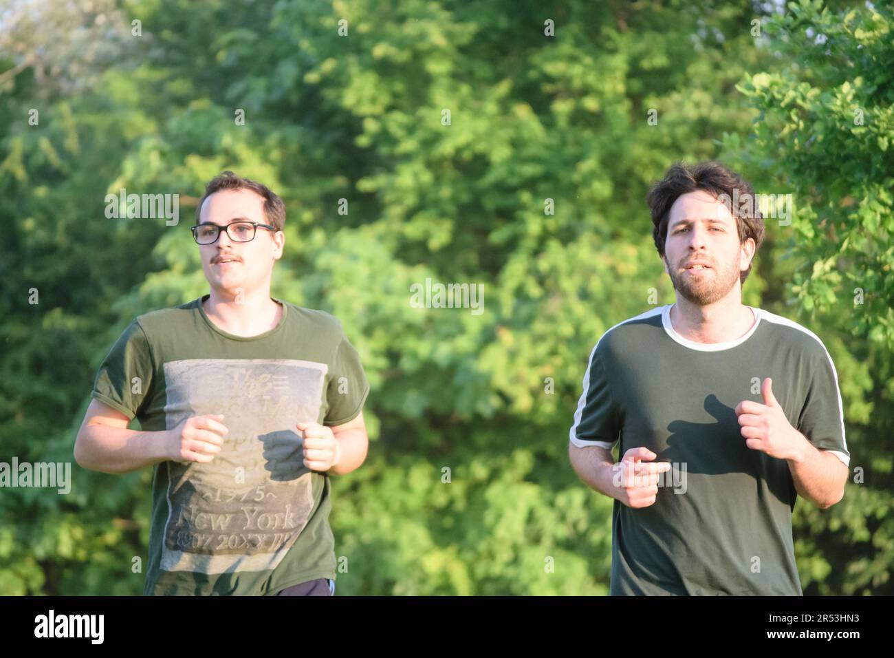 Due amici maschili che corrono con la t-shirt verde allenandosi nel parco nelle giornate di sole Foto Stock