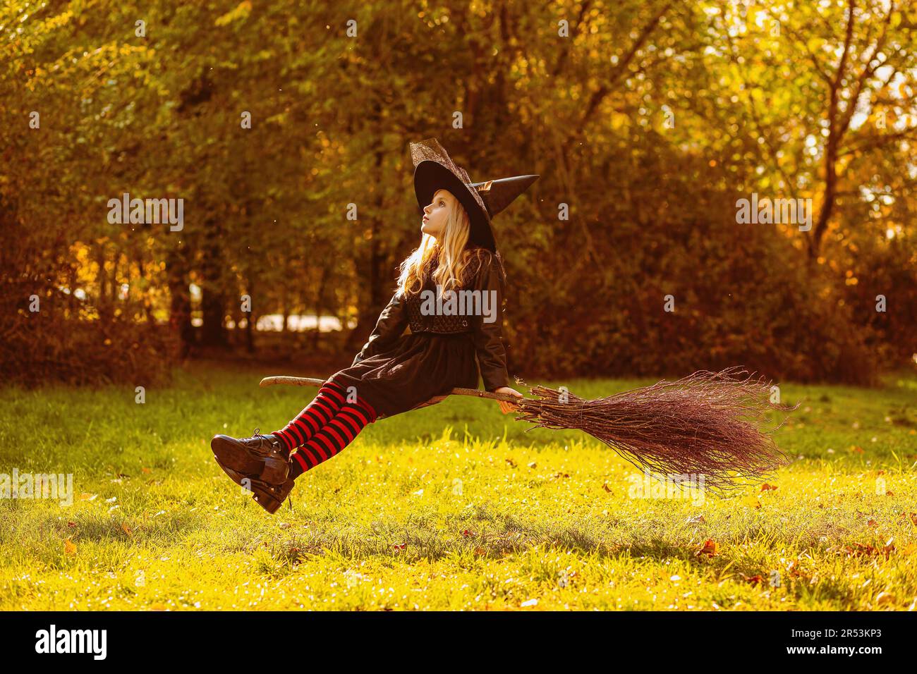 Una ragazza in costume da strega siede su una scopa galleggiante. Foto Stock