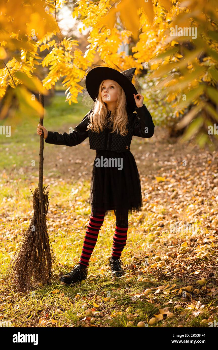 Una ragazza in costume da strega si alza con una scopa, che tiene sul cappello, in una foresta autunnale. Costume di Halloween Foto Stock