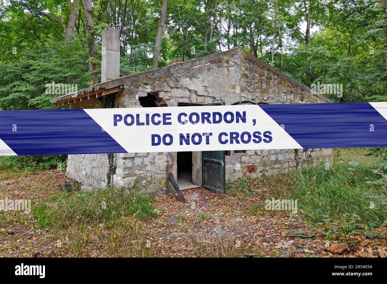 Casa di pietra abbandonata nel bosco con un nastro di polizia con scritto in esso 'cordone di polizia, non attraversare'. Foto Stock